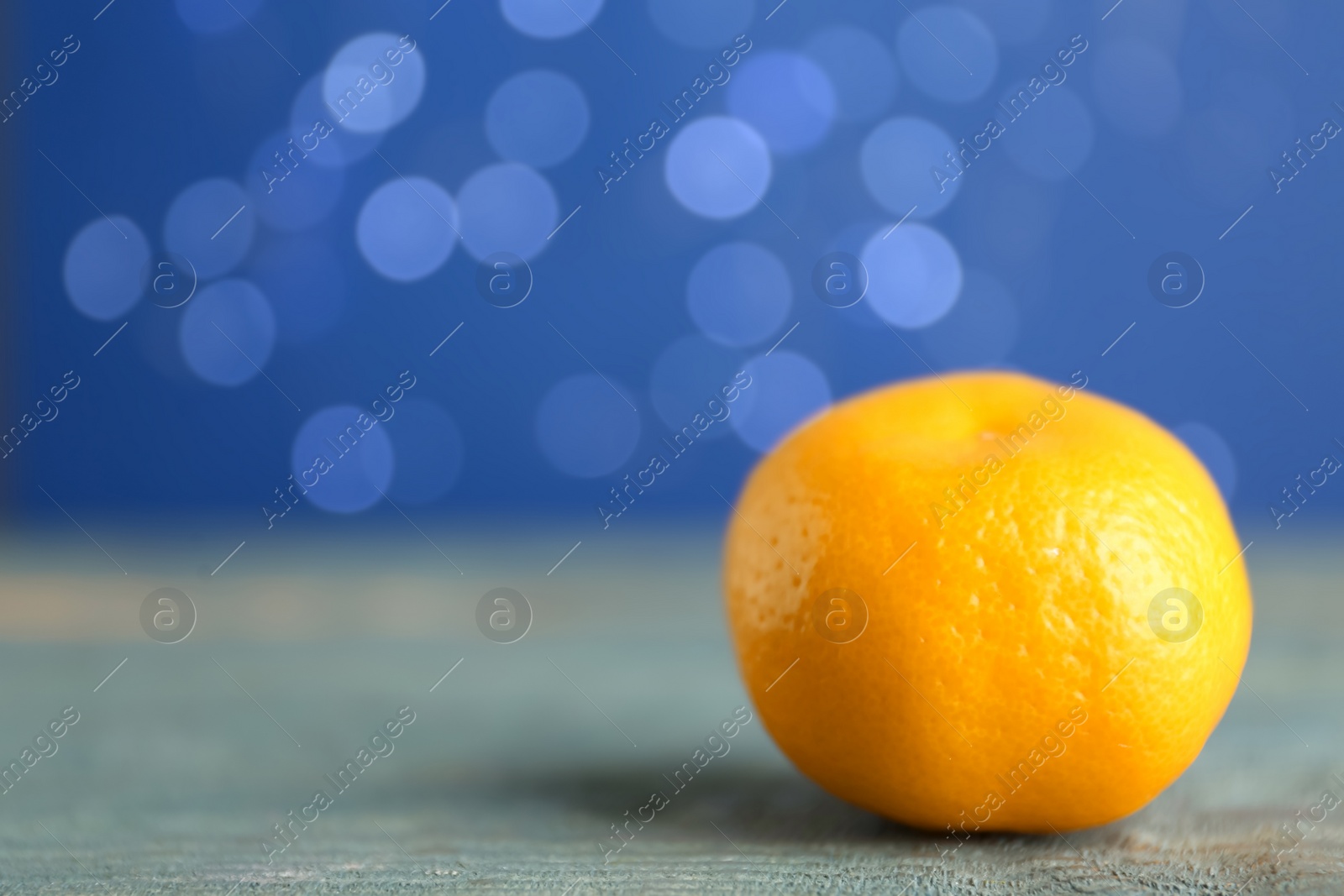 Photo of Tangerine on grey table against blurred lights, space for text