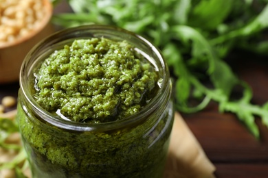 Photo of Jar of tasty arugula pesto on table, closeup