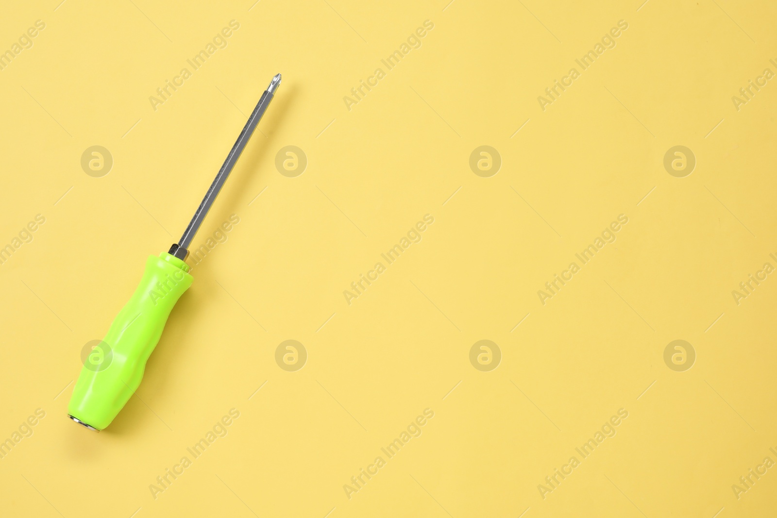 Photo of Screwdriver with green handle on light yellow background, top view. Space for text