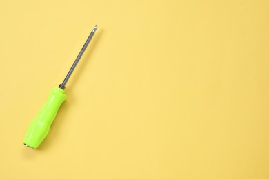 Photo of Screwdriver with green handle on light yellow background, top view. Space for text