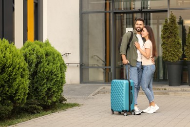 Photo of Long-distance relationship. Beautiful young couple with luggage hugging near building outdoors