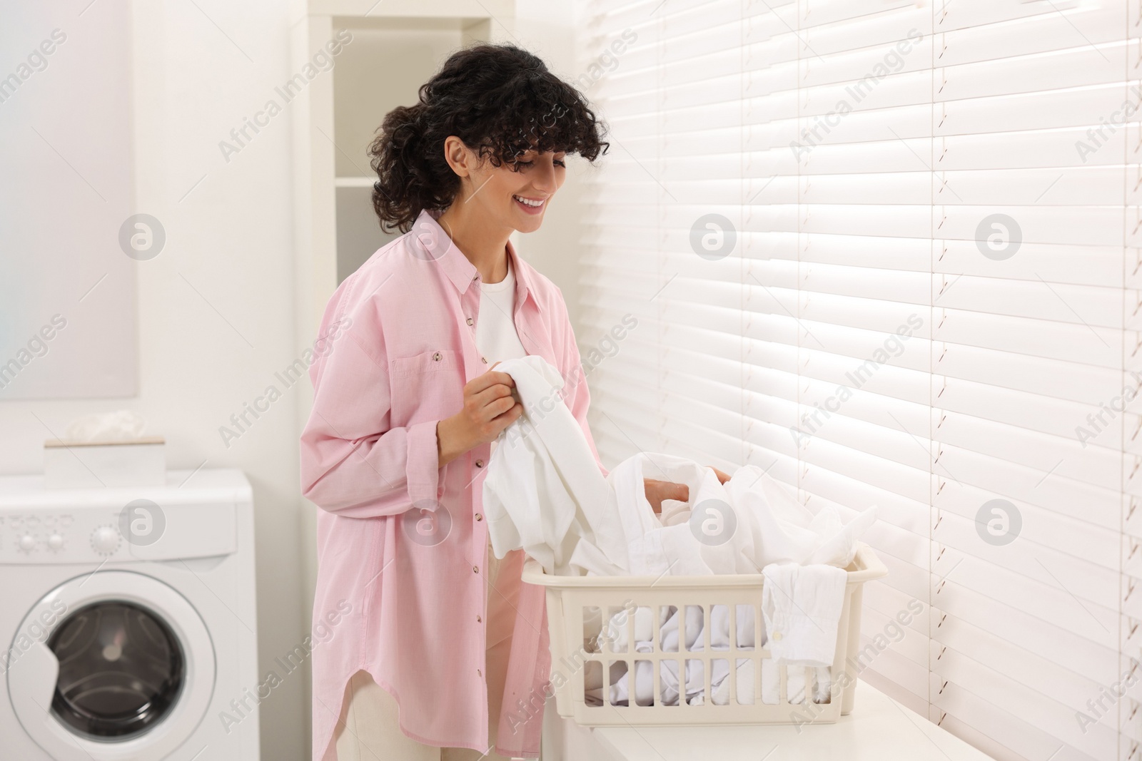 Photo of Happy woman with laundry near window indoors