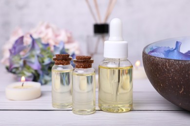 Photo of Spa composition. Bottles of essential oil and aromatic water with flowers in bowl on white wooden table, closeup