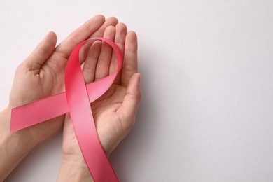 Woman holding pink ribbon on white background, top view with space for text. Breast cancer awareness concept