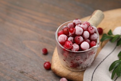 Photo of Frozen red cranberries in glass pot and green leaves on wooden table, closeup. Space for text