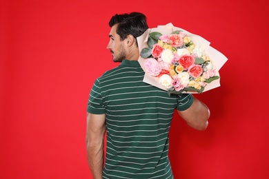 Young handsome man with beautiful flower bouquet on red background