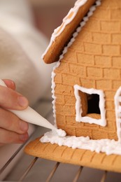 Photo of Woman decorating gingerbread house with icing, closeup