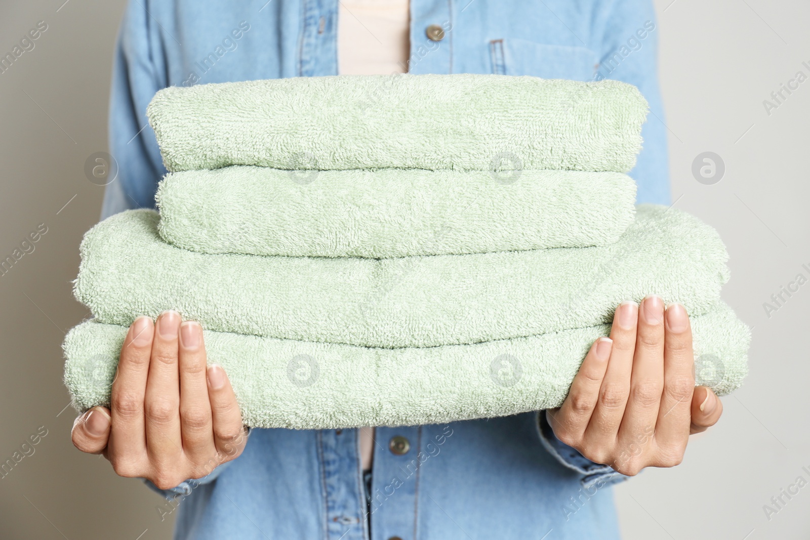 Photo of Woman holding stack of fresh towels on grey background, closeup