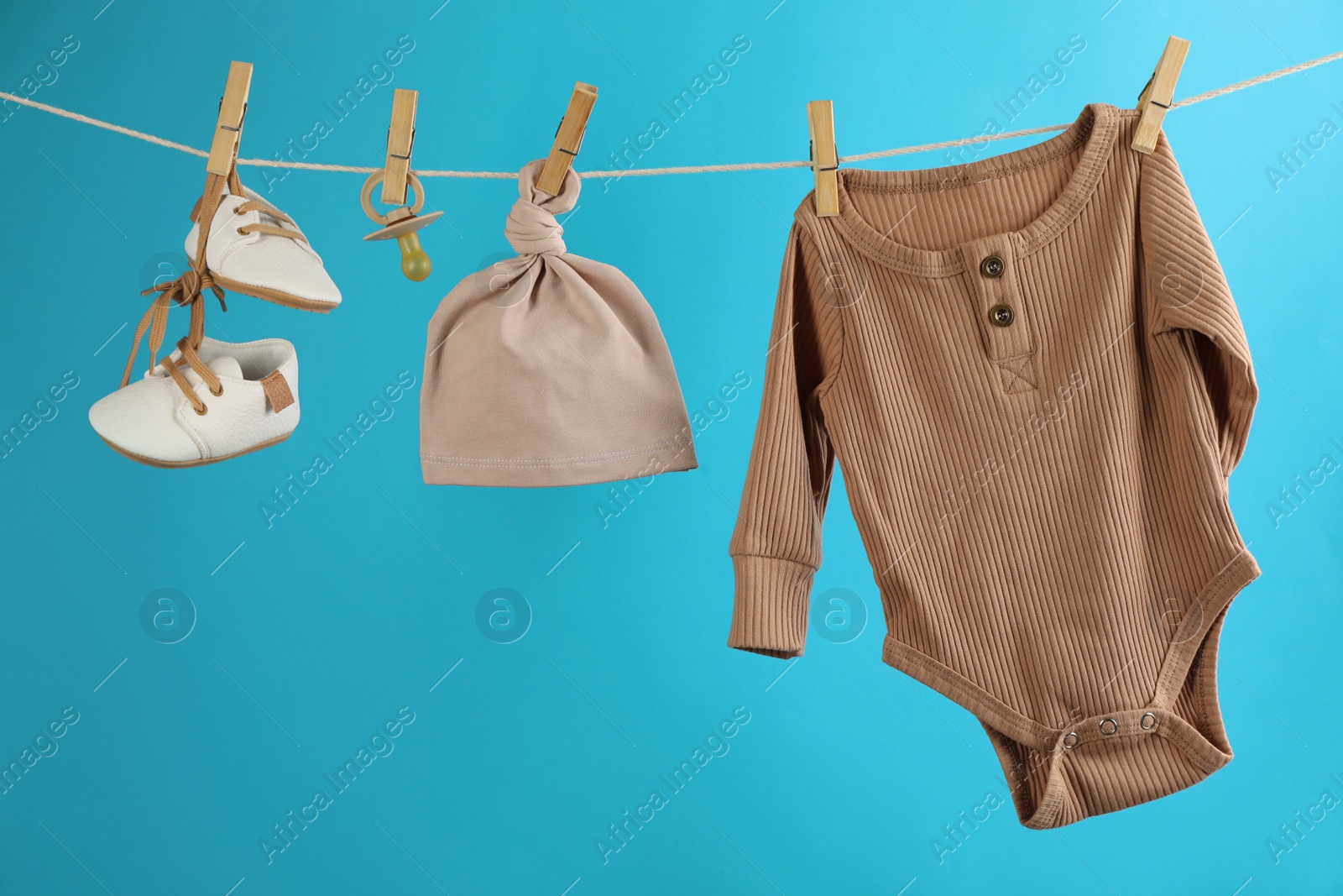 Photo of Baby clothes and accessories hanging on washing line against light blue background
