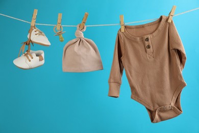 Baby clothes and accessories hanging on washing line against light blue background