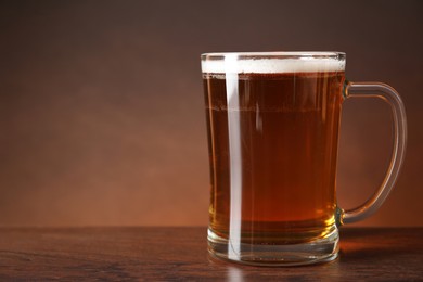 Mug with fresh beer on wooden table against brown background. Space for text