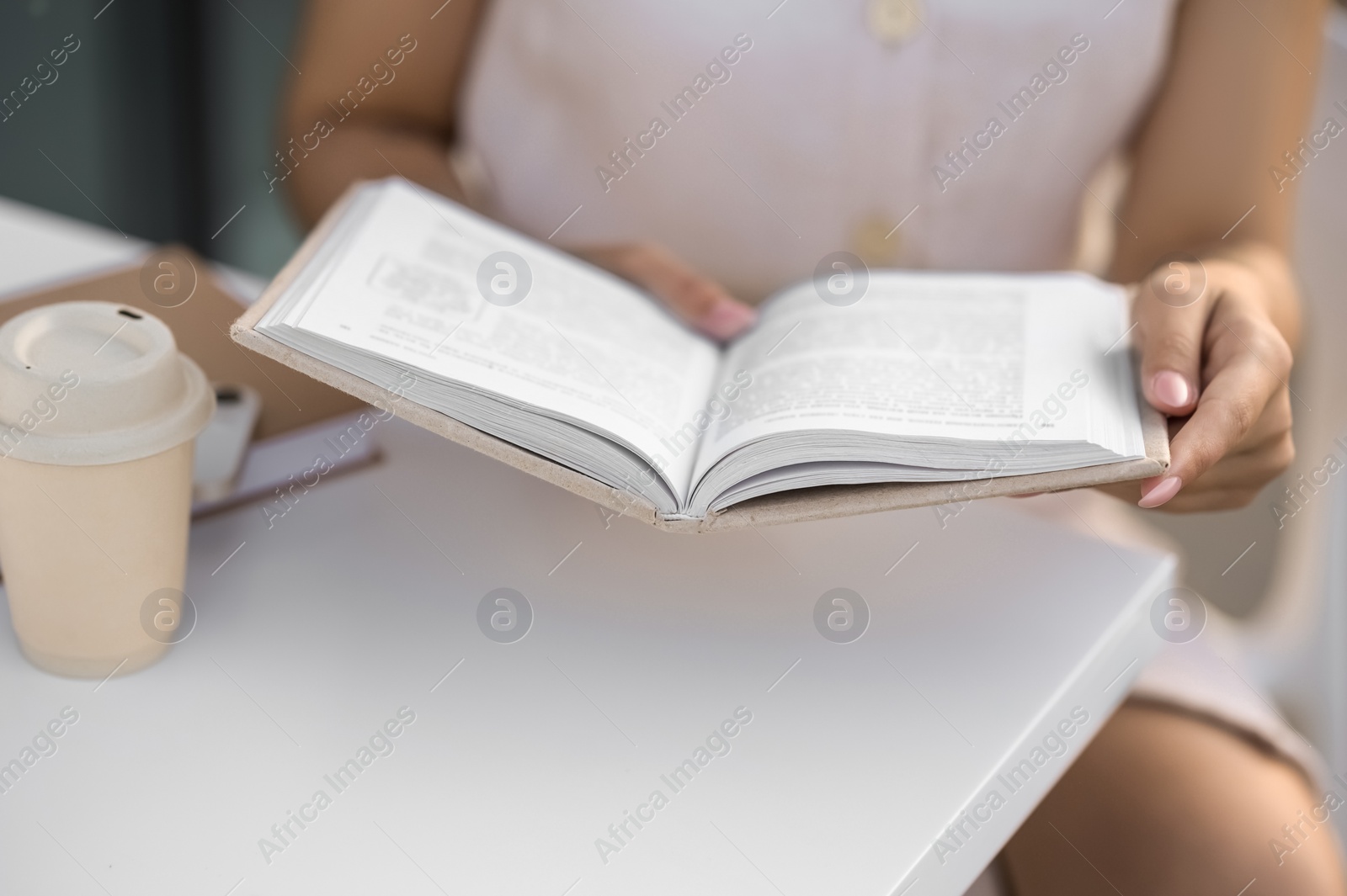 Photo of Woman with coffee reading book at white table outdoors, closeup