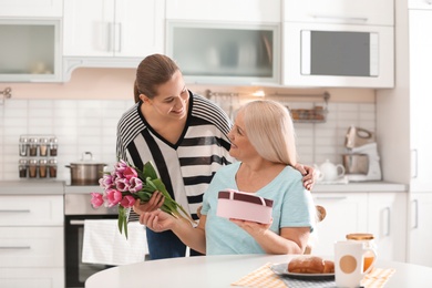 Daughter congratulating happy mature woman on Mother's Day at home