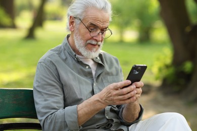 Photo of Portrait of happy grandpa with glasses using smartphone on bench in park