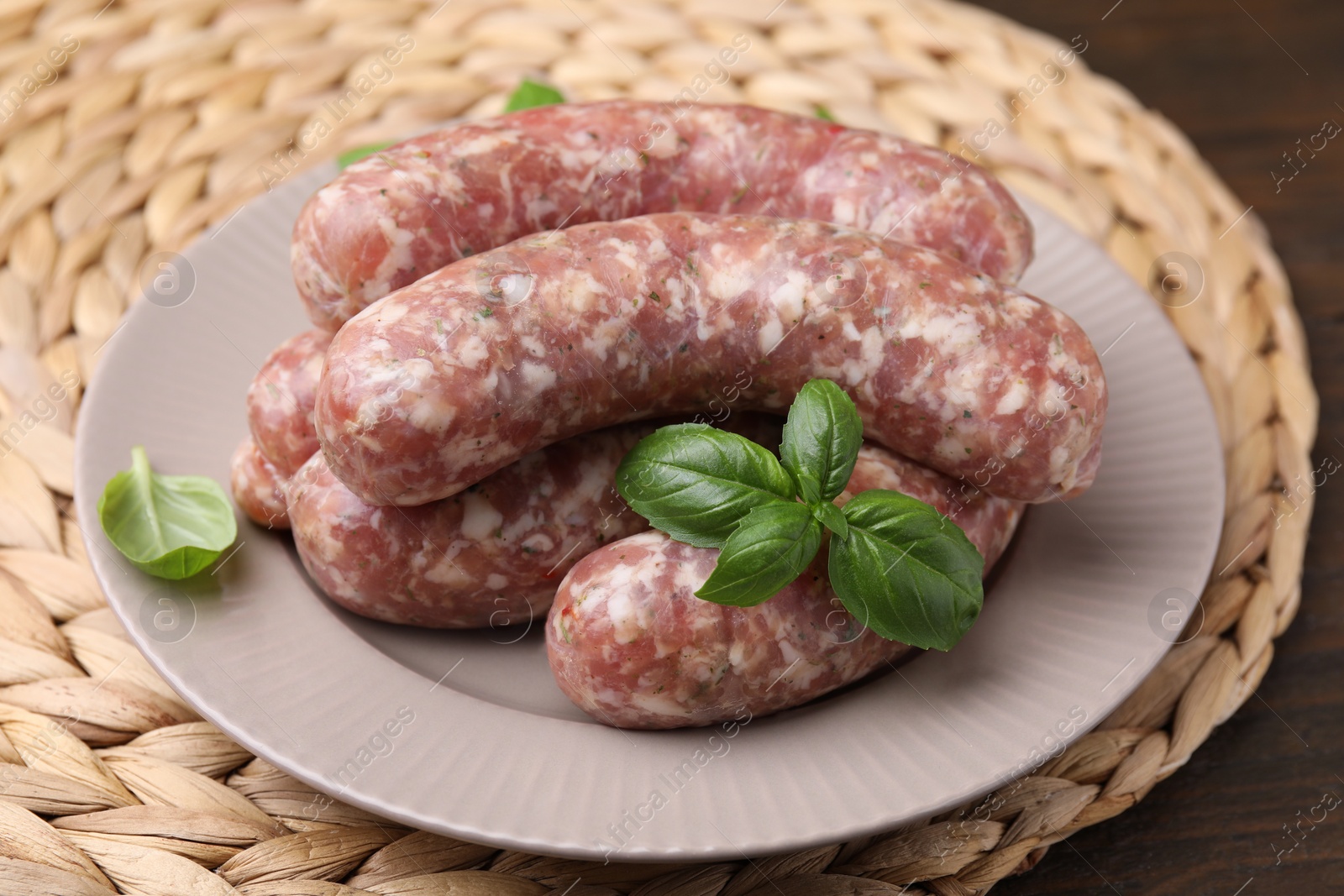 Photo of Raw homemade sausages and basil leaves on table, closeup