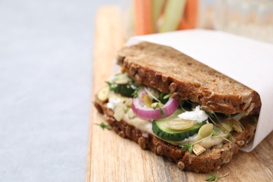 Photo of Tasty vegan sandwich with cucumber, onion, hummus and pumpkin seeds on light grey table, closeup. Space for text