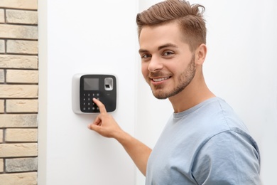 Photo of Young man entering code on alarm system keypad indoors