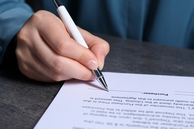 Woman signing document with pen at grey table, closeup