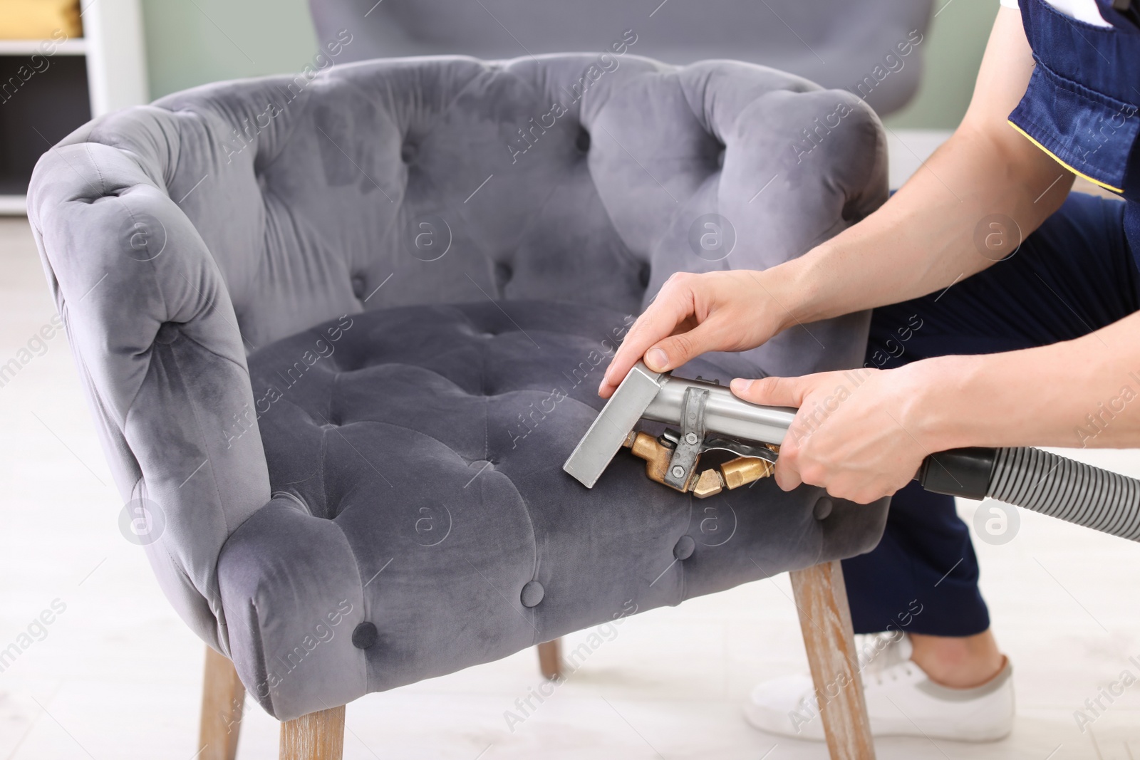 Photo of Male worker removing dirt from armchair with professional vacuum cleaner indoors, closeup