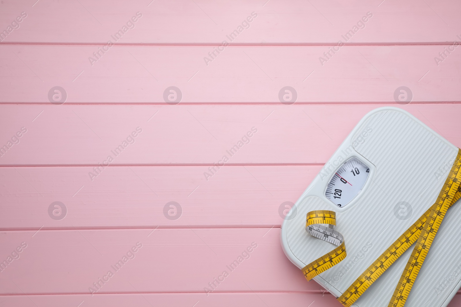 Photo of Bathroom scale, measuring tape and space for text on pink wooden floor, top view. Weight loss concept