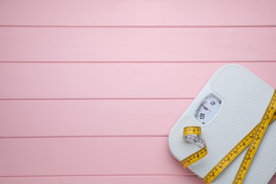 Photo of Bathroom scale, measuring tape and space for text on pink wooden floor, top view. Weight loss concept