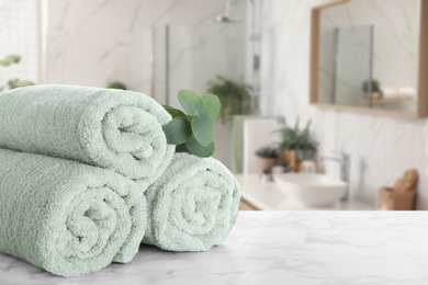 Image of Fresh towels and eucalyptus branch on marble table in bathroom. Space for text