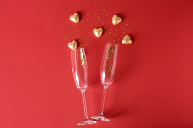 Champagne glasses and heart shaped candies in golden foil on color background, top view