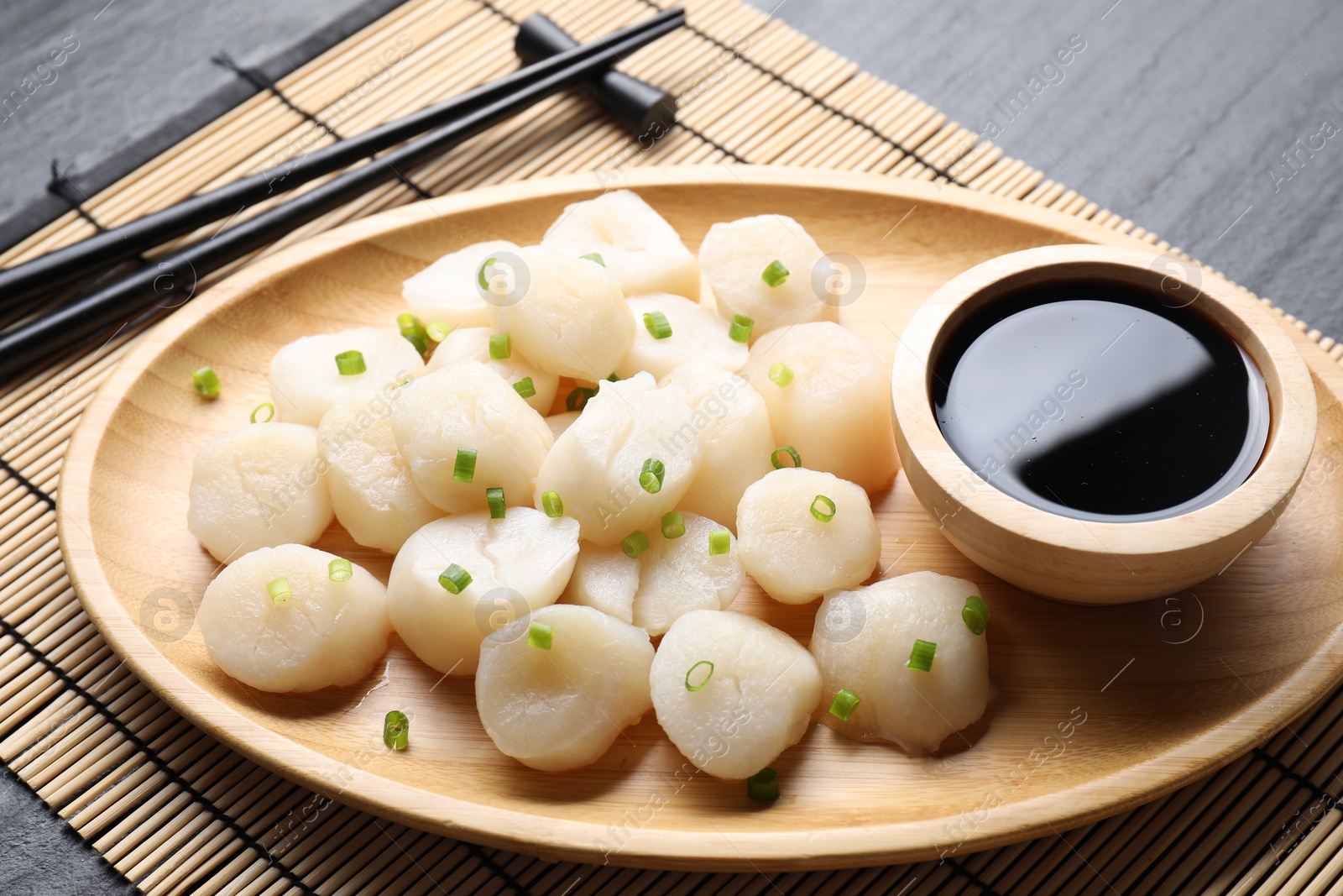 Photo of Raw scallops with green onion and soy sauce on dark table, closeup