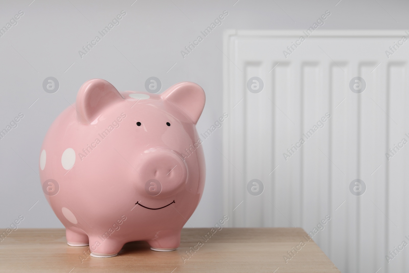 Photo of Piggy bank on wooden table near heating radiator, space for text