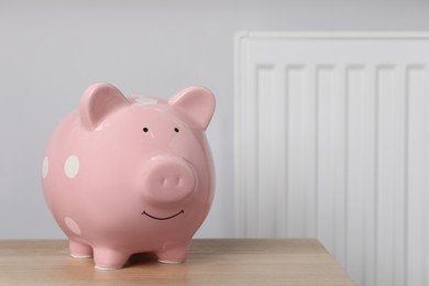 Photo of Piggy bank on wooden table near heating radiator, space for text