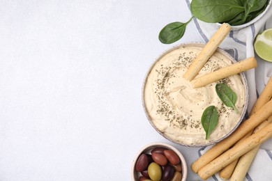 Photo of Delicious hummus with grissini sticks served on light grey table, flat lay. Space for text