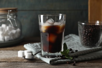 Photo of Glass of delicious iced coffee, mint and sugar cubes on wooden table