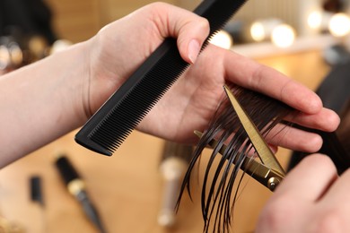 Hairdresser cutting client's hair with scissors in salon, closeup