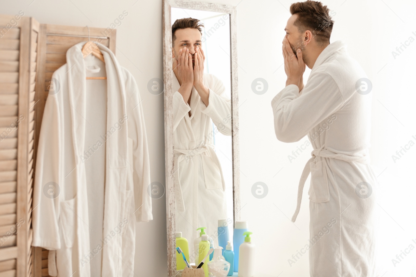 Photo of Young man looking at himself in mirror indoors