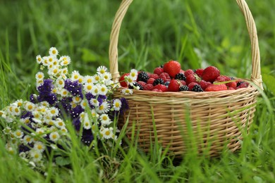 Photo of Wicker basket with different fresh ripe berries and beautiful flowers in green grass outdoors