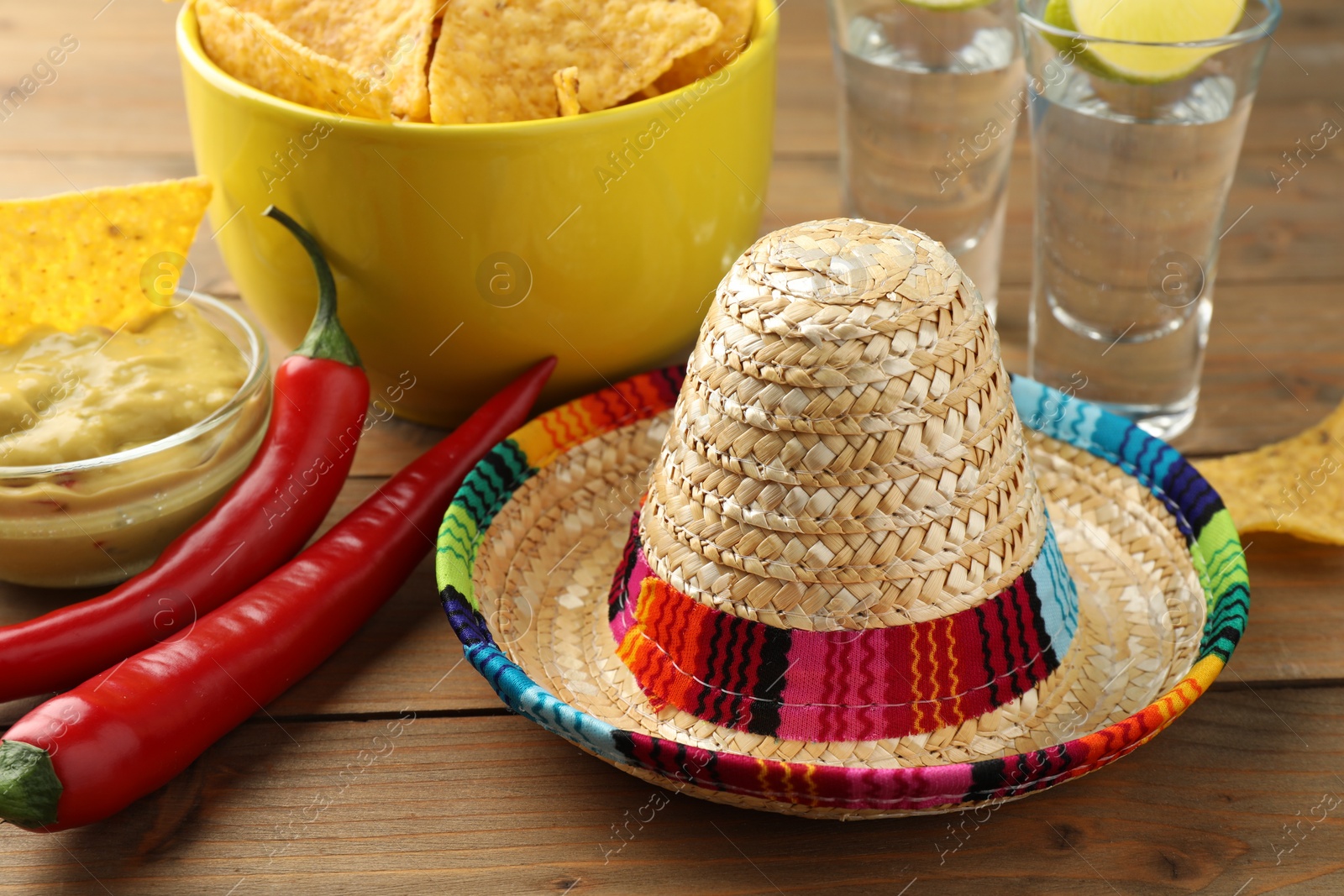 Photo of Mexican sombrero hat, tequila, chili peppers, nachos chips and guacamole on wooden table, closeup