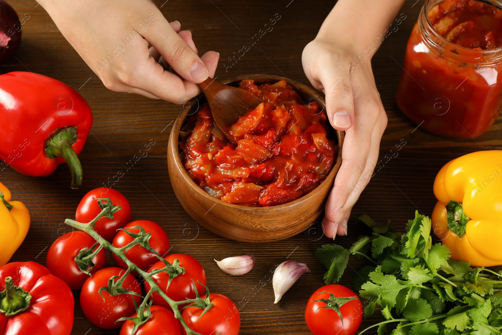 Photo of Woman with bowl of tasty lecho at wooden table, above view