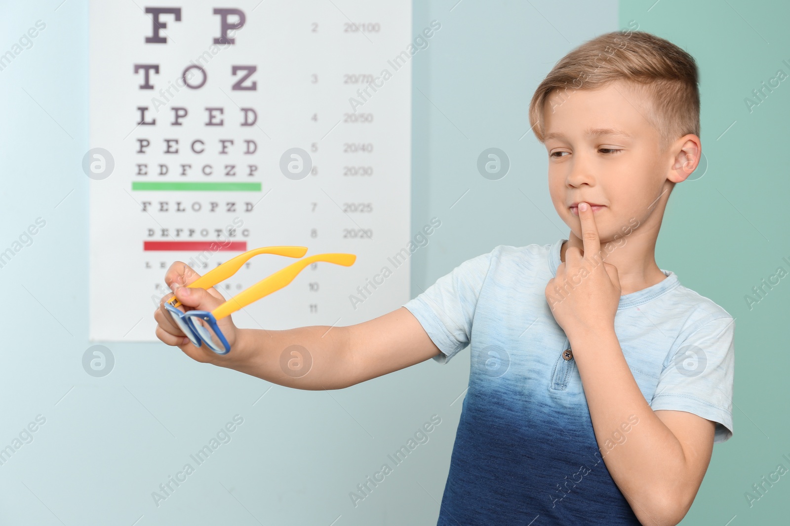 Photo of Cute little boy with eyeglasses in ophthalmologist office