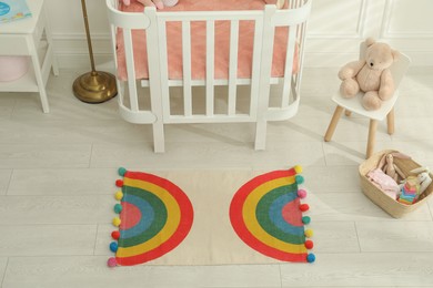 Stylish rug with rainbow on floor in baby room