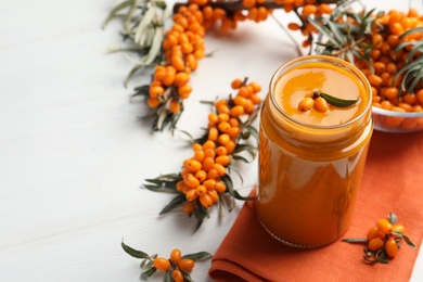 Photo of Delicious sea buckthorn jam and fresh berries on white wooden table. Space for text