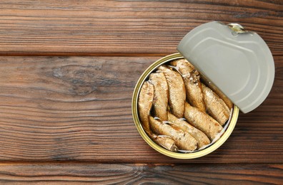 Photo of Open tin can of sprats on wooden table, top view. Space for text