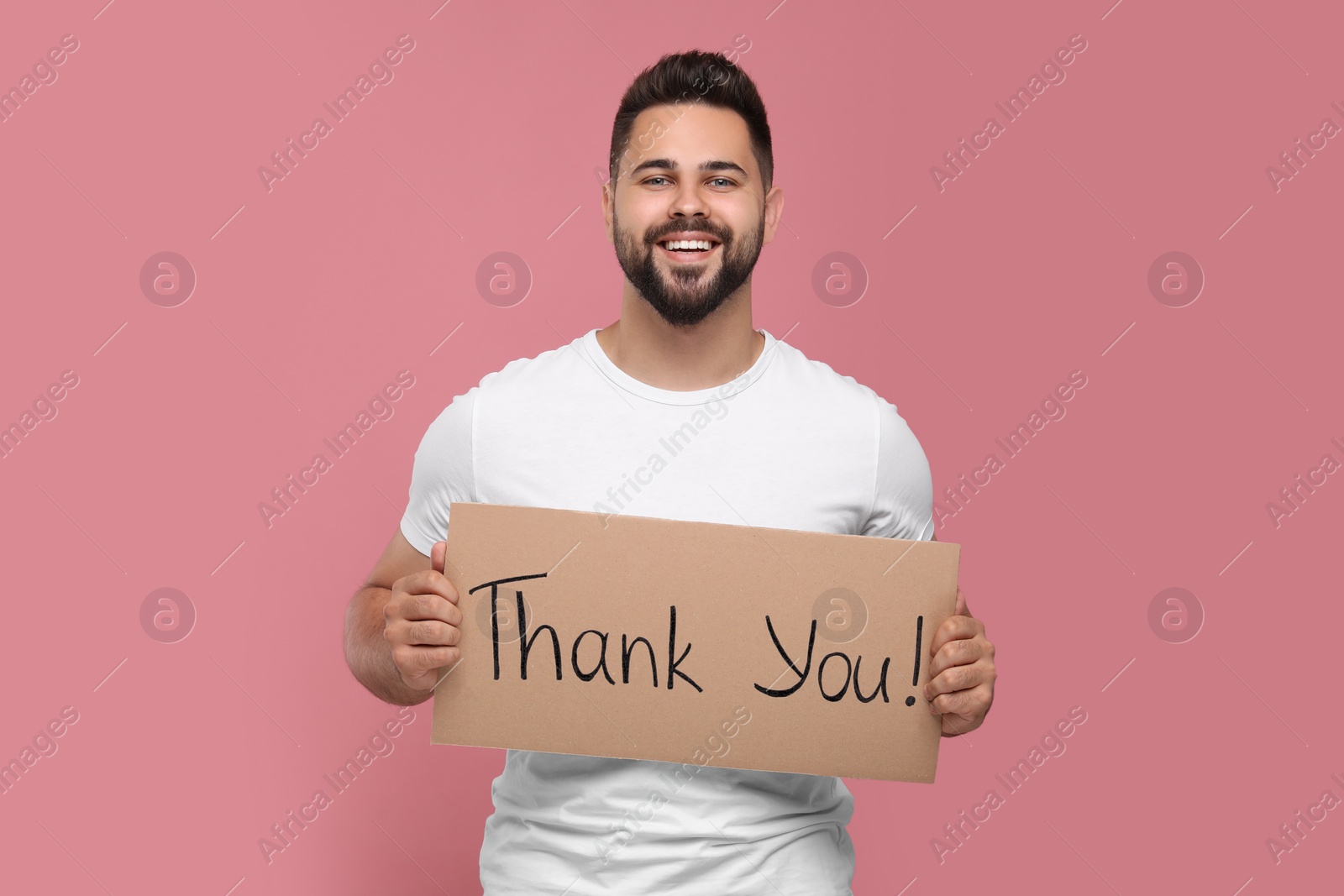 Photo of Happy man holding cardboard sheet with phrase Thank You on pink background