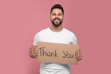 Photo of Happy man holding cardboard sheet with phrase Thank You on pink background