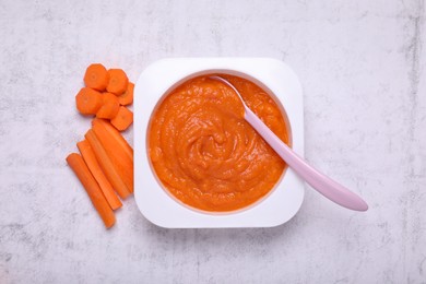 Photo of Container with healthy baby food and carrot on white textured table, flat lay
