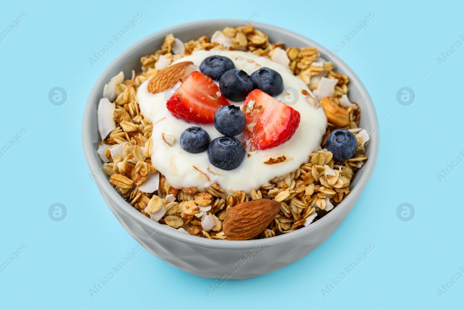 Photo of Tasty granola, yogurt and fresh berries in bowl on light blue background, closeup. Healthy breakfast