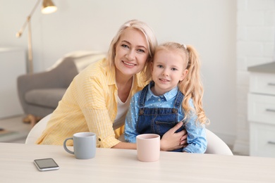 Photo of Portrait of mature woman and her granddaughter drinking tea at table indoors