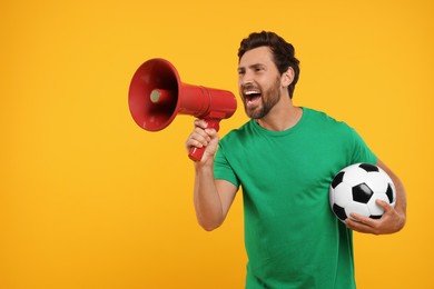 Photo of Emotional sports fan with soccer ball and megaphone on orange background