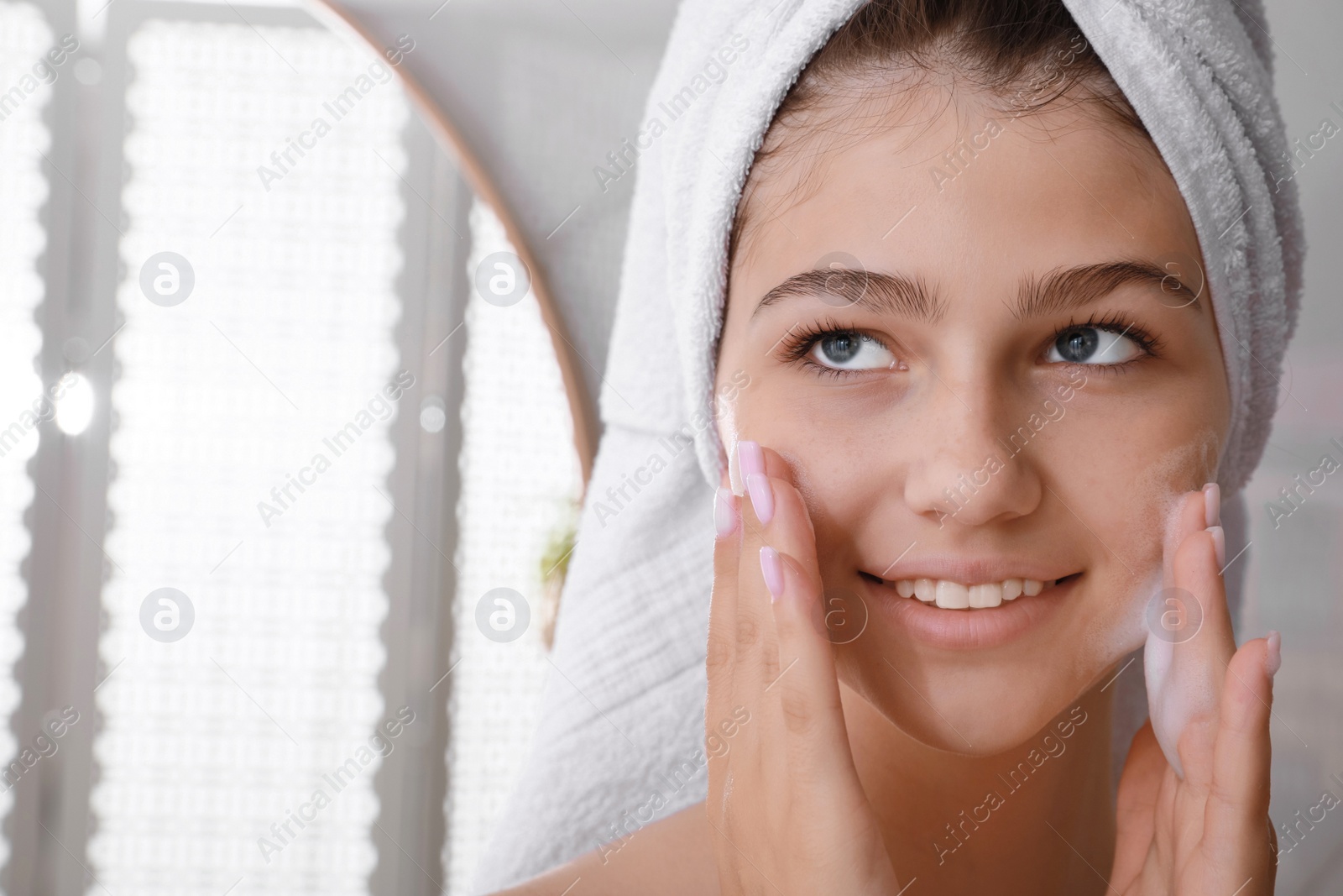 Photo of Beautiful teenage girl applying cleansing foam onto face in bathroom, space for text. Skin care cosmetic