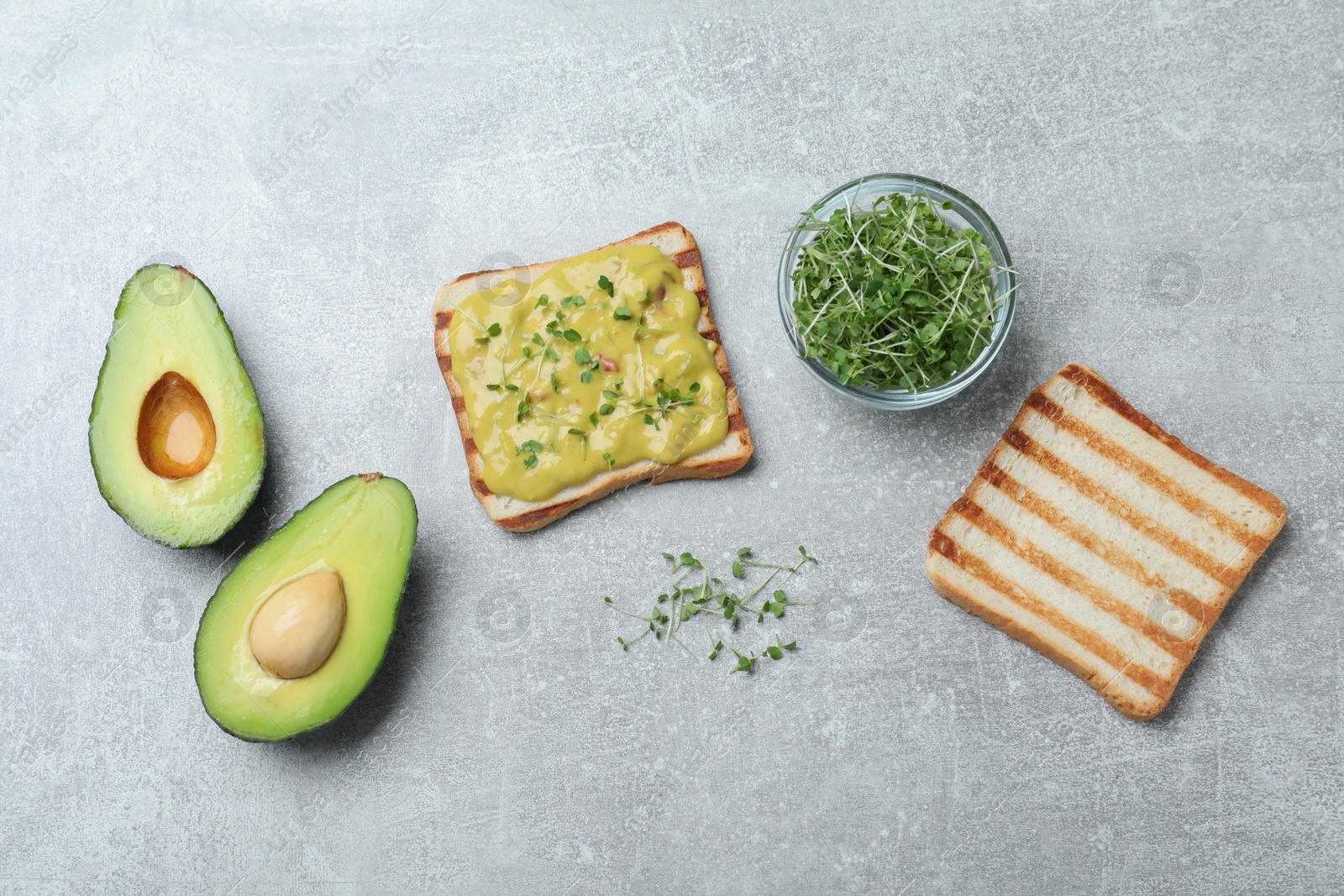 Photo of Delicious sandwich with guacamole and microgreens on grey table, flat lay