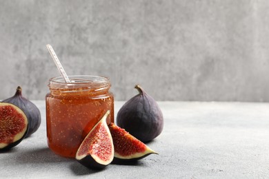 Photo of Glass jar with tasty sweet jam and fresh figs on light grey table. Space for text